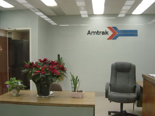 A station office with an Amtrak logo on the wall, a desk with poinsettias, and an empty office chair