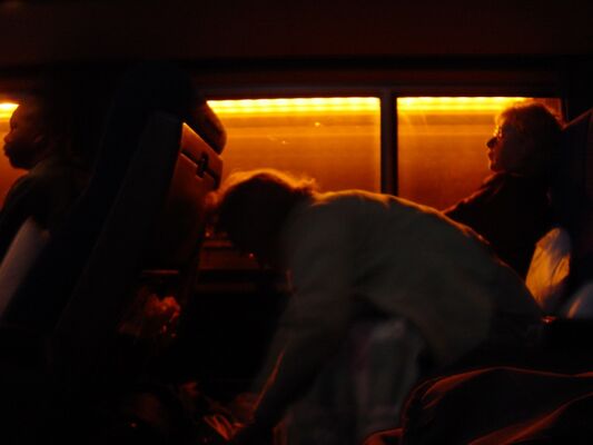Passengers gathering their things in a dark train car lit by orange light