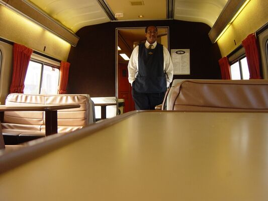 An Amtrak attendant in a vest standing at the end of an empty cafe car
