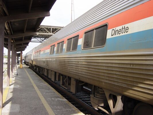 A silver Amtrak car with a red, white, and blue stripe, stopped at a station platform