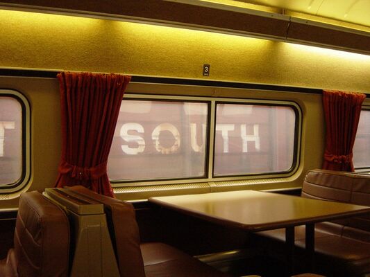 A dining car booth with red curtains, and the word South painted on a wall outside the window
