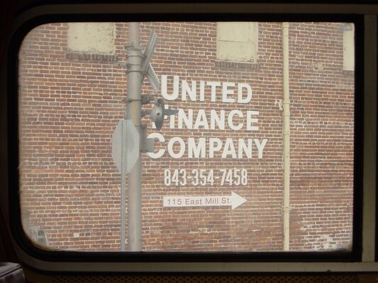 A painted United Finance Company sign on a brick wall, framed by the train window
