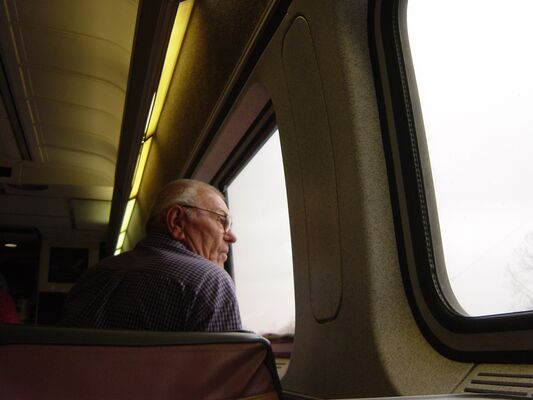 An older man in a train seat gazing out a bright window