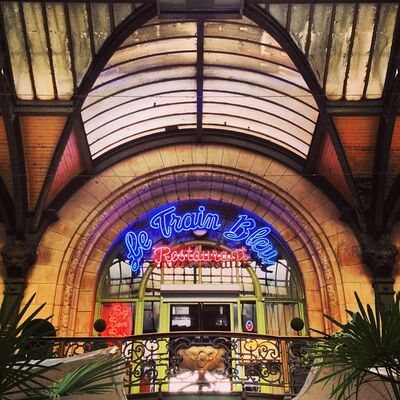The neon script sign of Le Train Bleu restaurant under the arched glass roof of the Gare de Lyon