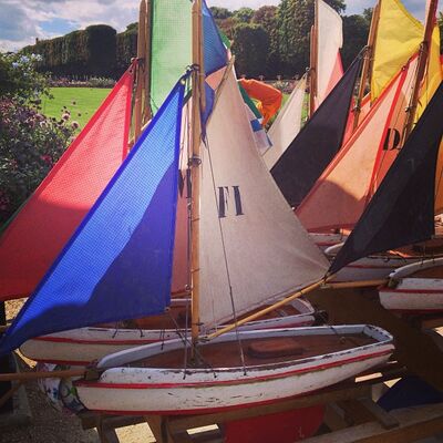Toy sailboats with bright red, blue, and yellow sails crowded together in a park
