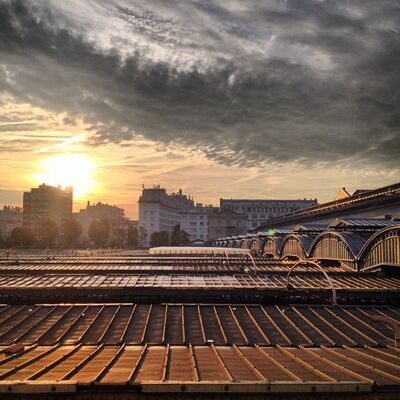 The sun rising under heavy clouds over the long platform roofs of the Gare de l’Est