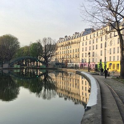 Apartment buildings and bare trees reflected in the still water of the Canal Saint-Martin