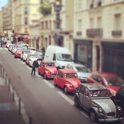 A line of red and gray Citroën 2CVs stuck in traffic on a narrow Paris street