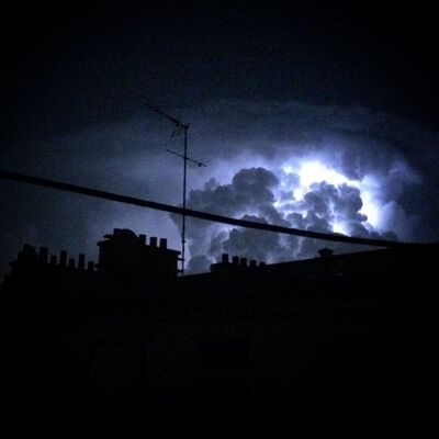 Lightning glowing inside a storm cloud above dark rooftops and a TV antenna