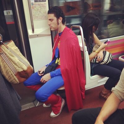A man dressed as Superman dozing on a seat in a Metro car