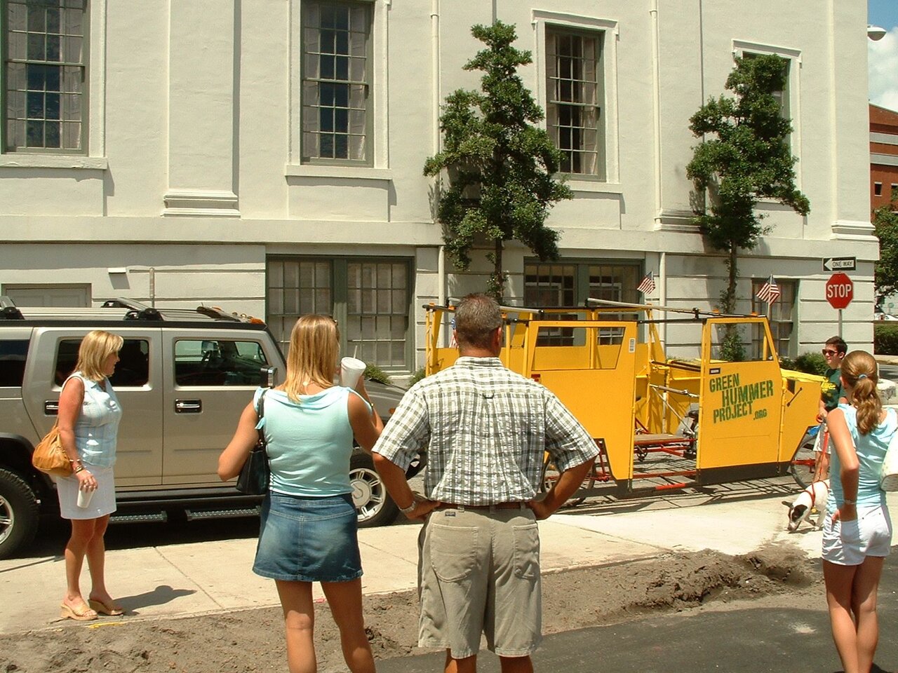 Onlookers watching the Green Hummer, parked behind a real Hummer H2 outside a white building