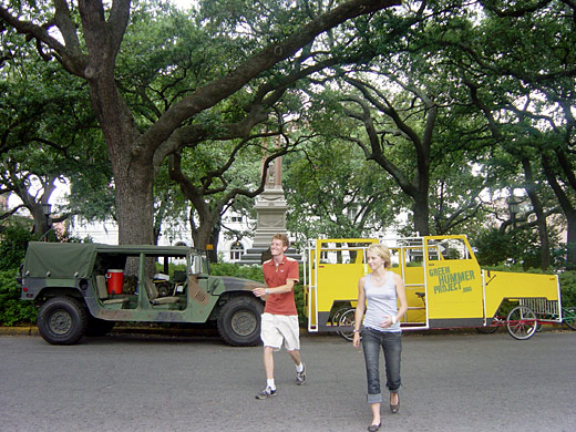The Green Hummer parked beside an army Humvee under live oaks, as two people walk past