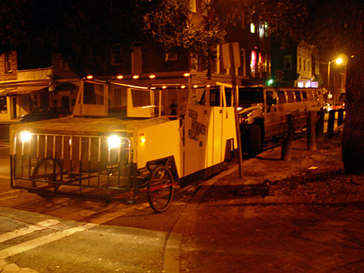 The Green Hummer at night, its lights on, parked in front of a white stretch Hummer limousine