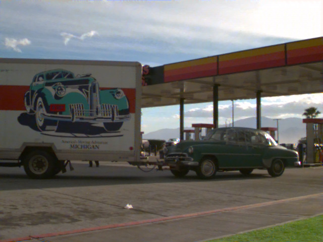 A moving truck and an old car at a gas station